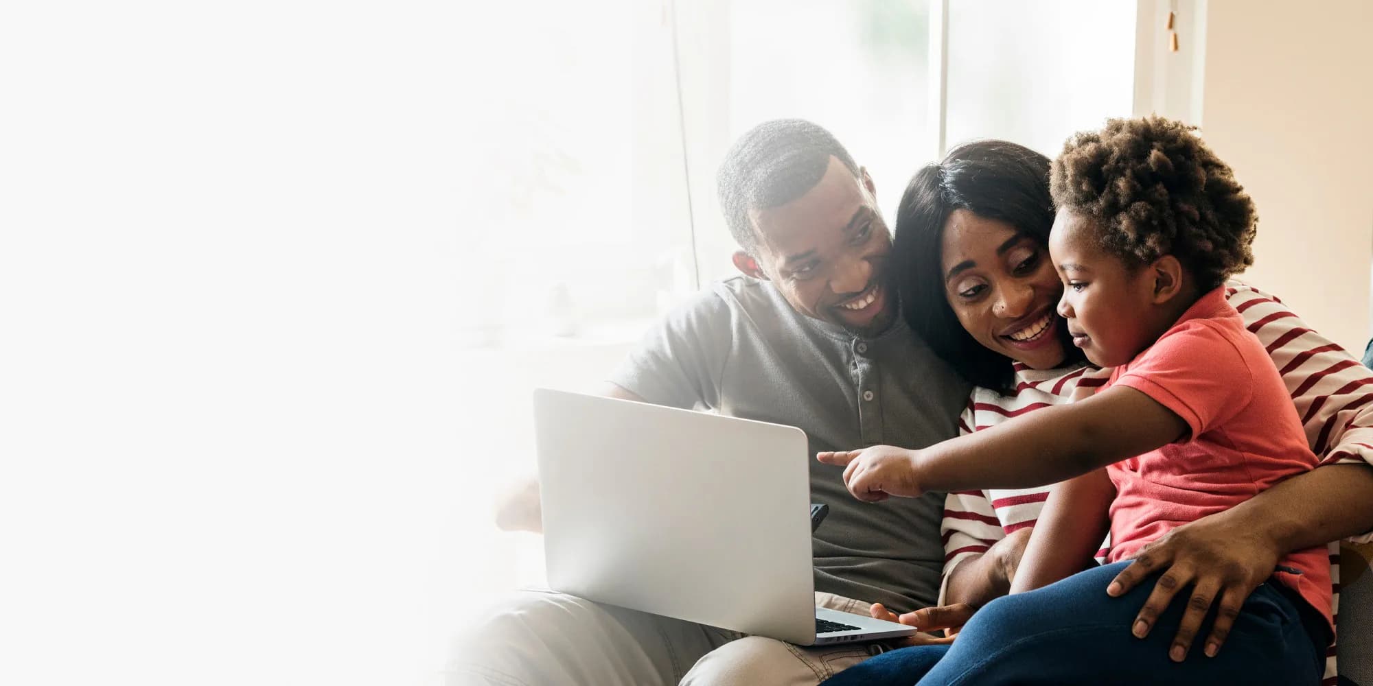 A mother, a father and their young child smiling at a laptop together on a sofa.